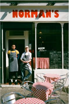 two men standing in front of a restaurant with red and white checkered tablecloths