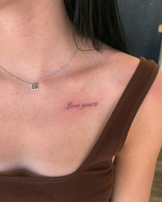 a woman wearing a brown shirt has a small tattoo on her chest that says love yours