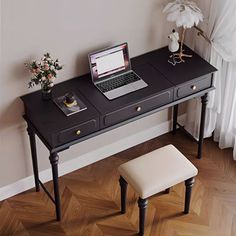 a laptop computer sitting on top of a black desk next to a white stool and window