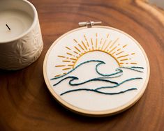 a wooden table topped with a embroidery kit next to a white cup and candle holder