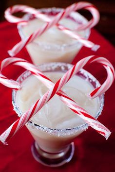 two glasses filled with candy canes on top of a red tablecloth covered table