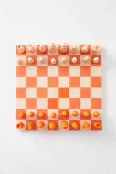 an orange and white checkerboard board with chess pieces on the top, in front of a white background