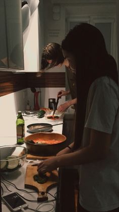 two people preparing food in a kitchen on top of a counter next to each other