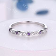 a white gold ring with three diamonds and purple sapphires on it's side