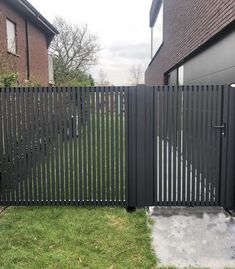 a black metal fence in front of a brick building with grass and trees behind it