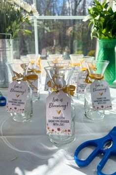 several small glass vases with flowers in them on a table next to blue scissors