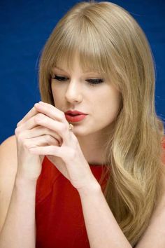 a woman with long blonde hair is holding her hand to her face and looking down