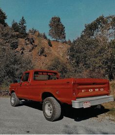 a red pick up truck parked on the side of a road next to some trees