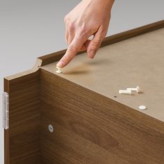 a hand is pointing at some screws on a wooden cabinet door that's open