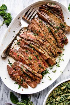 grilled steak on a white platter with parsley garnish and a fork