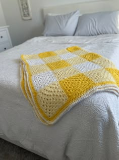 a yellow and white crocheted blanket sitting on top of a neatly made bed