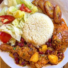 a white plate topped with rice, meat and veggies on top of a wooden table