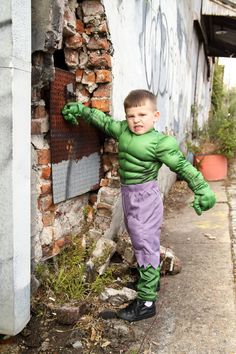 a young boy dressed as the hulk in front of a brick wall with graffiti on it