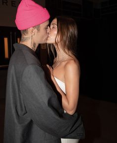 a man and woman kissing each other in front of a building at night with the lights on