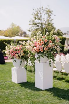 two white vases with flowers on them sitting in the middle of an outdoor ceremony