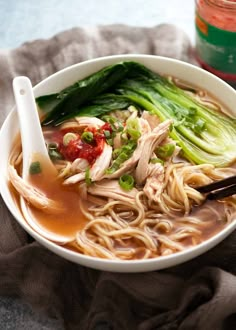 a white bowl filled with noodles, meat and veggies next to a jar of sauce