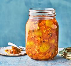 a glass jar filled with pickles next to a plate and spoon on a table