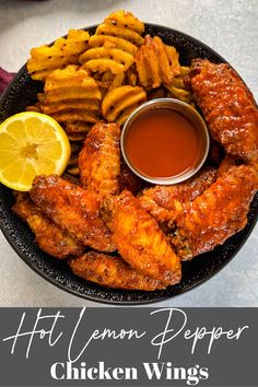 chicken wings with dipping sauce and lemon wedges on a black plate next to some french fries