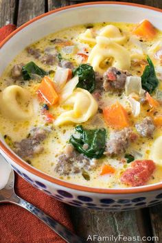 a bowl of pasta soup with meat, cheese and spinach in it on a wooden table