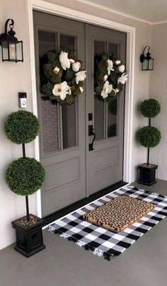 a black and white checkered rug is on the front porch with two potted plants