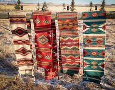 four different colored rugs hanging on a fence in the snow with mountains in the background