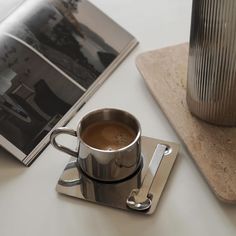 a cup of coffee sitting on top of a table next to a book and coaster