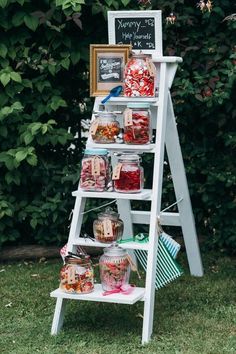 a white shelf filled with jars and containers on top of grass next to trees in the background