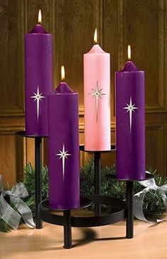 three purple candles sitting on top of a table next to a christmas wreath and ribbon