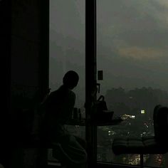 a woman sitting at a table in front of a window with the city lights behind her