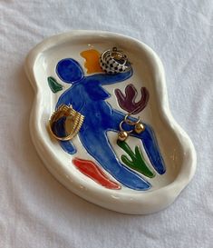 a ceramic dish with a person holding a ring on it's side and other items in the shape of a heart