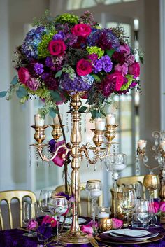 a fancy table setting with purple and red flowers in a tall centerpiece on top of it