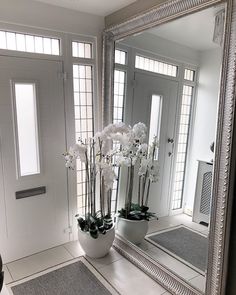 a large silver mirror sitting on top of a white floor next to a vase filled with flowers