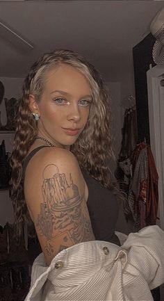 a woman with tattoos on her arm standing in a closet holding a bag and looking at the camera