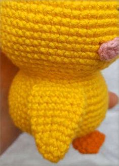 a yellow crocheted toy with a pink nose is held in the palm of someone's hand