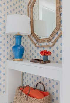 a blue vase sitting on top of a white table next to a basket and lamp