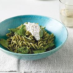 a blue bowl filled with pasta and spinach on top of a white table cloth