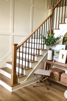 there is a plant on the table next to the stair case in this room with white walls and wood flooring