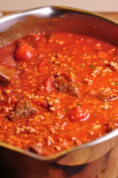 a pot filled with meat and tomato sauce on top of a wooden table next to a knife