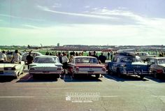 several old cars are parked in a parking lot with people standing around them and looking at them