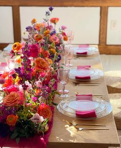 the table is set with pink and orange flowers in vases, plates, and napkins