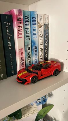 a red toy car sitting on top of a book shelf next to some other books