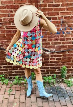 a woman standing in front of a brick wall wearing a hat and dress with flowers on it