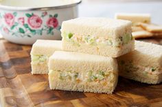 three sandwiches stacked on top of each other next to a bowl of crackers and a spoon