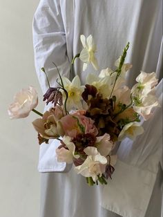 a person wearing a white shirt holding a bouquet of flowers in their hands with both hands