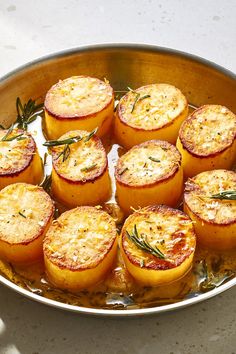 a metal pan filled with cooked tomatoes covered in cheese and rosemary sprinkled on top