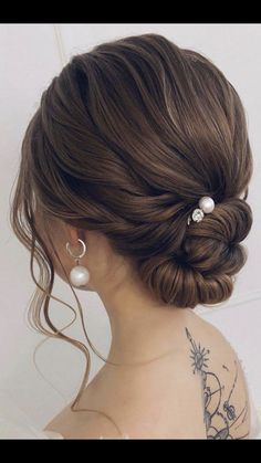 a woman with her hair in a low bun and pearl earrings on her left shoulder