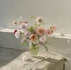 a vase filled with pink and white flowers sitting on top of a cement block next to a window