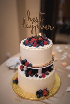 a three tiered cake with berries and blueberries on top is sitting on a gold plate