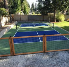 an outdoor tennis court with blue and green net on it's sides, surrounded by trees