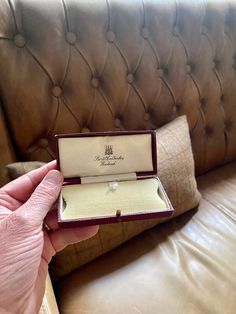 a person holding an open ring box on top of a leather couch in a living room